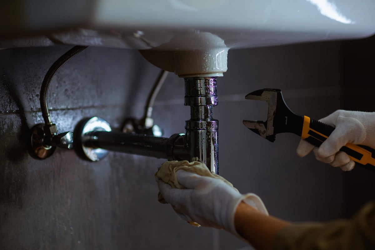 Professional plumber working on plumbing under a sink using adjustable wrench