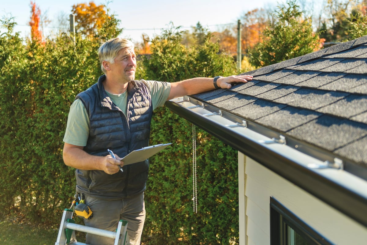 Professional roofer standing on steps inspecting house roof